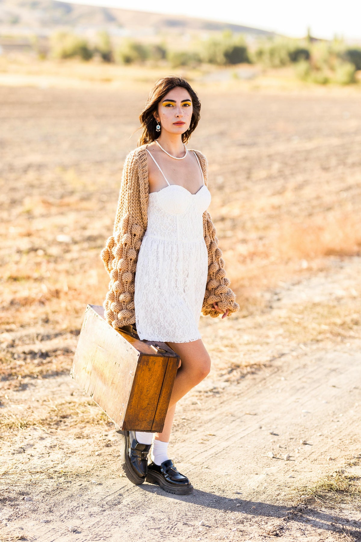 Woman wearing a beige knit cardigan over a white dress with ankle boots